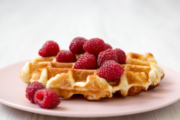 Belgian waffle with raspberries on pink plate over white wooden surface, side view. Close-up.