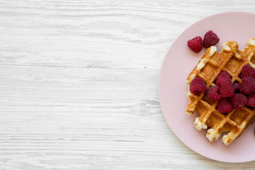 Traditional belgian waffle with raspberries on pink plate on white wooden background, overhead view. Flat lay, top view, from above. Copy space.