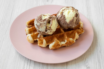 Traditional belgian waffle with icecream on pink plate over white wooden surface, side view. Close-up.