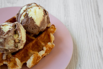 Traditional belgian waffle with icecream on pink plate over white wooden surface, side view. Close-up.