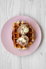 Traditional belgian waffle with icecream on pink plate over white wooden surface, top view. Close-up.