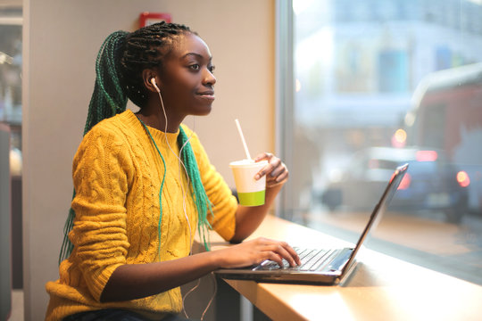 Girl having lunch in a bar, listening music and using her laptop
