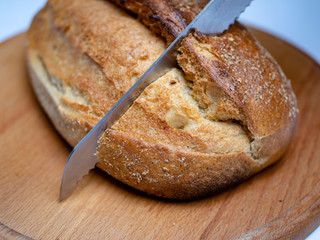 Whole grain bread put on kitchen wood plate with a chef holding gold knife for cut. Fresh bread on...
