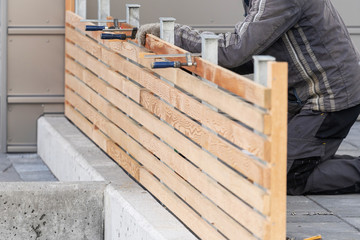 Unrecognizable man repairing new wooden fence near house