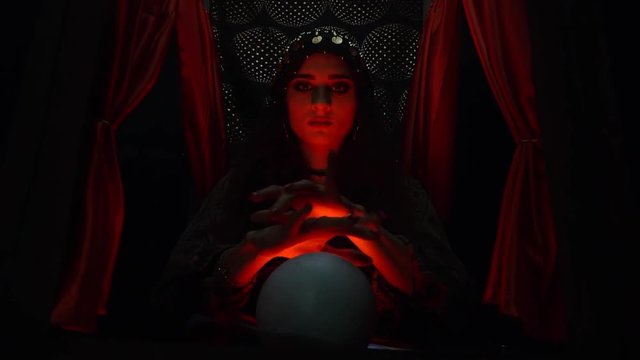 Creepy witch sitting in front of the crystal ball in red light
