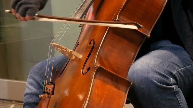 Street musician playing the cello close up view. Cellist in gloves gently bows strings