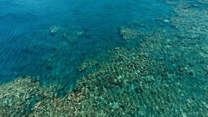 Fototapeta na wymiar stunning aerial drone image of a a small fishing boat entering an a sea ocean anchorage in a channel next to a coral reef in crystal clear azure blue water at a remote isolated tropical island