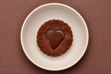 Heart-shaped chocolate chip cookies with toffee, in a white plate, on a brown paper background.