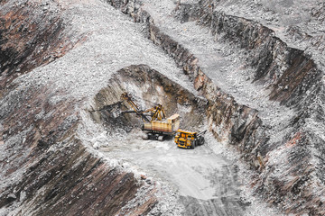 Large orange mining truck and excavator in a quarry. Iron ore extraction. Heavy mining equipment. View from above on opencast mining quarry for the extraction of ironstone magnetite ores 