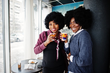Two curly hair african american woman wear on sweaters with cups of tea posed at cafe indoor.