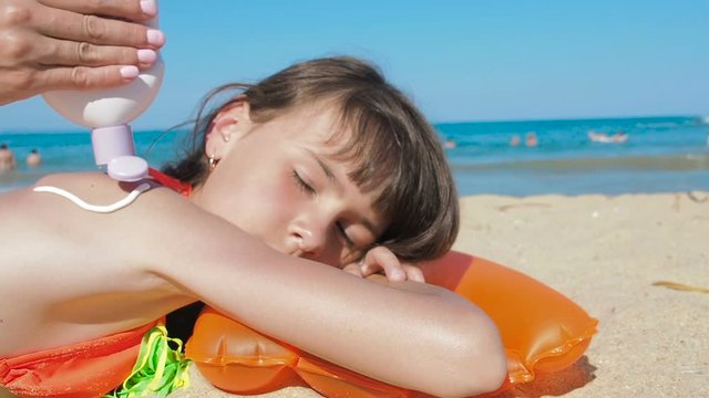 Spread sunblock on the body. Mother smears sunscreen on the back of a little girl on a sunny day at the beach.
