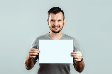 A young, attractive man holding a blank white A4 sheet, on a light background. mockup, layout, copy...