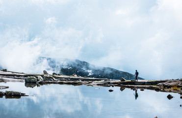 Silhouette of backpacker walking towards the edge of rocky lake. near Trolltunga, Norway