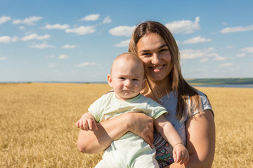 Fototapeta na wymiar Mother with child in wheat, Young happy family in wheat field smiling and enjoying the sun