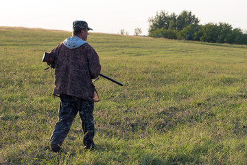 Silhouette of a hunter with a gun in the reeds against the sun, an ambush for ducks with dogs	