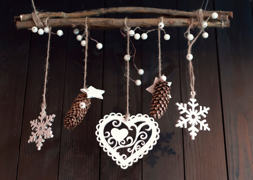 Christmas decor on a wooden brown wall background. Cones, heart, berries and stars hanging on the ropes on the branch.