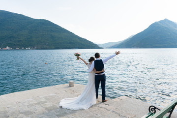 newlyweds stand on the pier with their hands raised