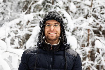 Man in fur winter hat with ear flaps smiling portrait. Extreme in the forest