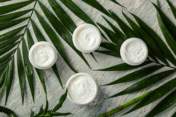 Obraz na płótnie Canvas Jars of cream with tropical leaves on light table