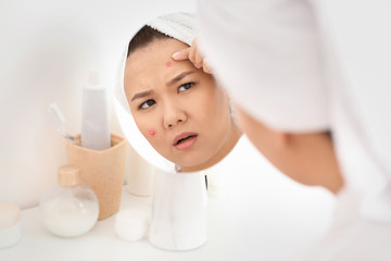 Fototapeta na wymiar Portrait of young Asian woman with acne problem looking in mirror