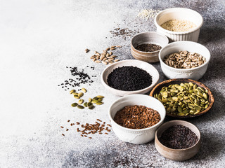 Various seeds - sesames, flax seed, sunflower seeds, pumpkin seed, poppy, chia in bowls on a gray background. Copy space.
