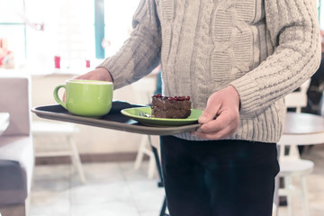 Elderly man carrying a tray with a cup of cappuccino and cake in a cafe.