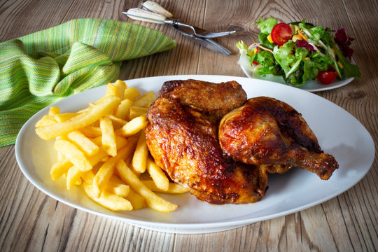 Halbes H&uuml;hnchen mit Pommes auf wei&szlig;em Teller