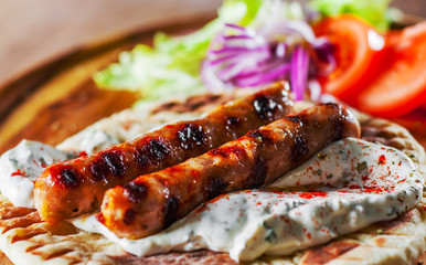 grilled meat sausages with pita bread and vegetables salad and tzatziki dip on wooden board