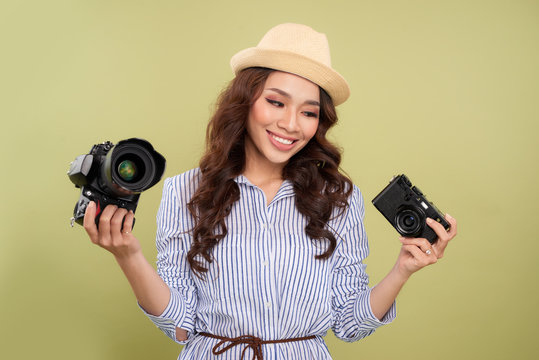 Young Woman Comparing Professional And Compact Cameras On A Solid Background