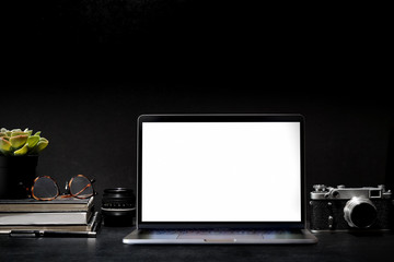 Dark creative  photographer desk with vintage camera, lens and blank screen laptop