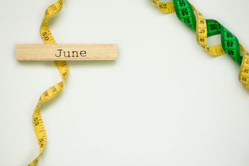 wooden calendar set on june with centimeter tape isolated on white background. Slimming marathon