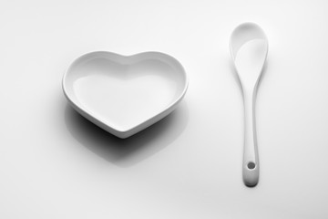 Minimalism. Heart saucer and ceramic spoon on a white background. For design on Valentine's Day, wedding, romantic dinner.