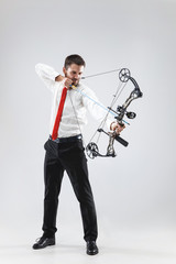Businessman aiming at target with bow and arrow, isolated on gray studio background. The business, goal, challenge, competition, achievement concept