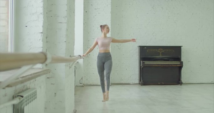 Graceful classic ballet dancer practicing developpe exercise at barre during rehearsal in ballet studio. Ballerina performing different choreographic exercises and dance moves in dance studio.