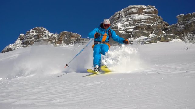 a skier rides down the slope making turns. snow splatter, no trace. on the background of beautiful rocks, blue sky and white snow. camera bottom view. Super slow motion