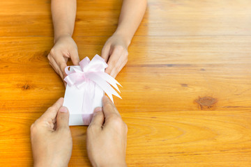 Two persons hands giving and receiving a present gift box on table.