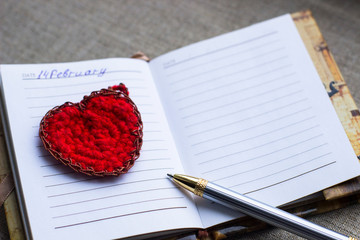 Valentines day background- red heart and silver pen are on the page of the diary on grey matting background, flat lay, copy space. Mothers day, other celebration or planning and dream concept. 