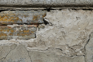 Large diagonal crack in the old concrete wall through which you can see the bricks
