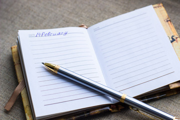 Valentines day background- silver pen are on the page of the diary on grey matting background, top view, flat lay, copy space. Mothers day, other celebration or planning and dream concept. 