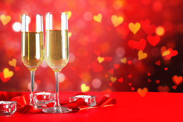 Conceptual image with two champagne flute glasses over red heart shaped bokeh lights. Romantic dinner for st Valentine's day. Close up, copy space. Colorful background for different romantic occasions
