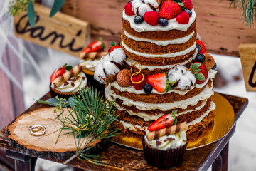 Wedding cake with fruit and an old wooden table with decorations and rings during a wedding ceremony in winter on snow in the middle of a forest covered with fresh snow