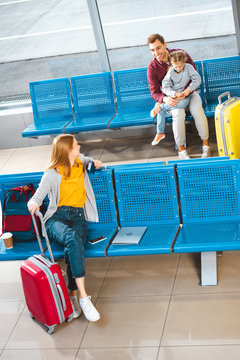 happy father sitting with daughter in airport near woman with luggage