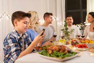 technology, holidays and people concept - happy boy with smartphone having family dinner party at home