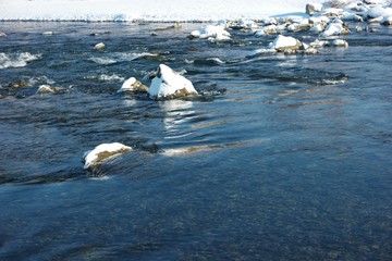 Snow-covered stones in a mountain river on a sunny winter day, background
