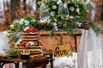 Wedding cake with fruit and an old wooden table with needles of cones and leaves during a wedding ceremony in winter on snow in the middle of a forest covered with fresh snow