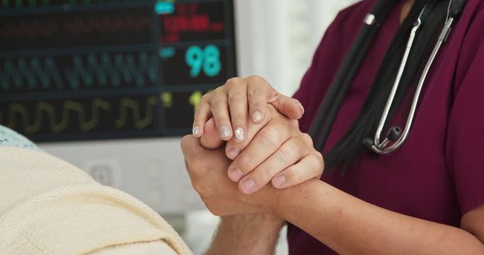 Close up on hands of doctor or nurse comforting male patient in hospital bed