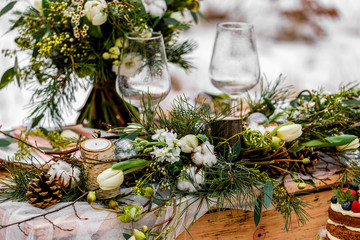 Wedding old wooden table with a flower-filled decoration and placement with glasses at a wedding ceremony in winter on snow in the middle of a forest covered with fresh snow...