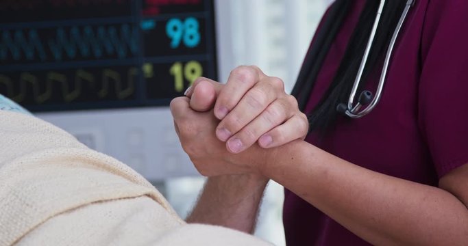 Close up on hand of female doctor or nurse comforting man in hospital bed