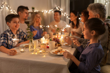 celebration, holidays and christmas concept - happy family with sparklers having fun at dinner party at home