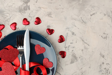 table setting. Blue plate with a knife and fork and red hearts on a light concrete background. Valentine's Day. place for text. view from above